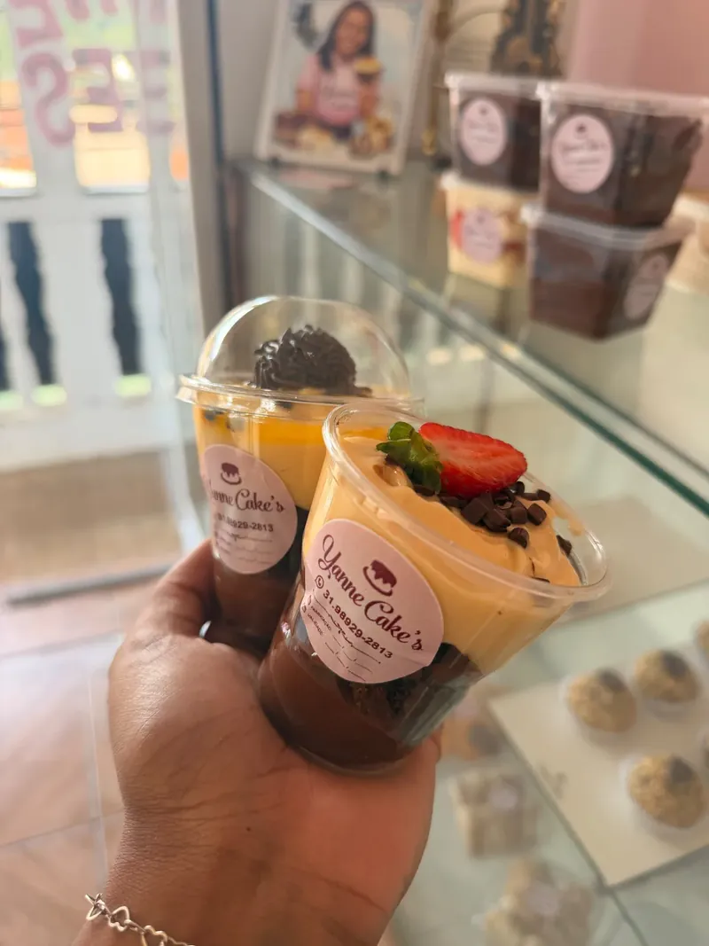 Mão segurando sobremesas no copinho com creme, chocolate e morango